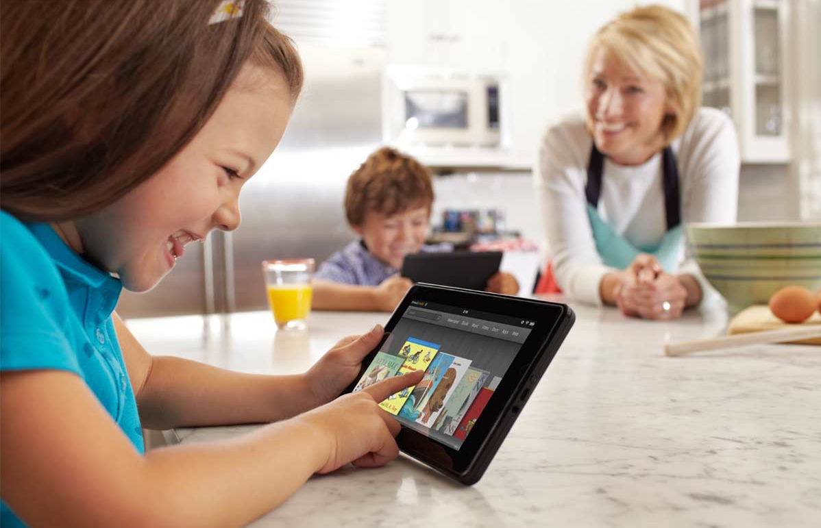 Dans la cuisine, des enfants jouent gaiement sur leurs tablette sous la surveillance d'un adulte